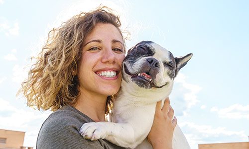 Happy woman holding bulldog. Horizontal view of woman with pet outdoors. Lifestyle with animals.